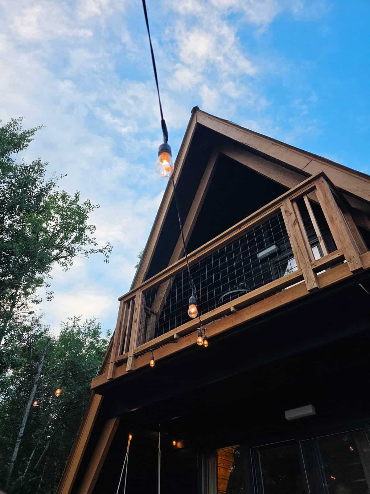 Close-up exterior view of an A-frame cabin with balcony and string lights