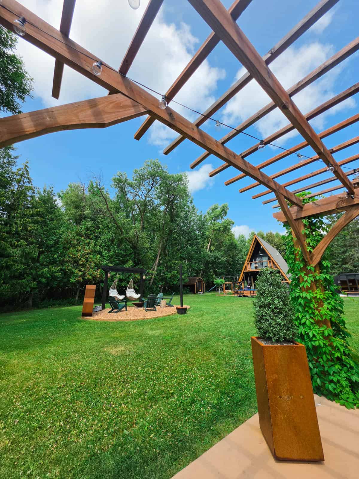 Wide view of the A-frame cabin lawn with firepit seating and outdoor pergola