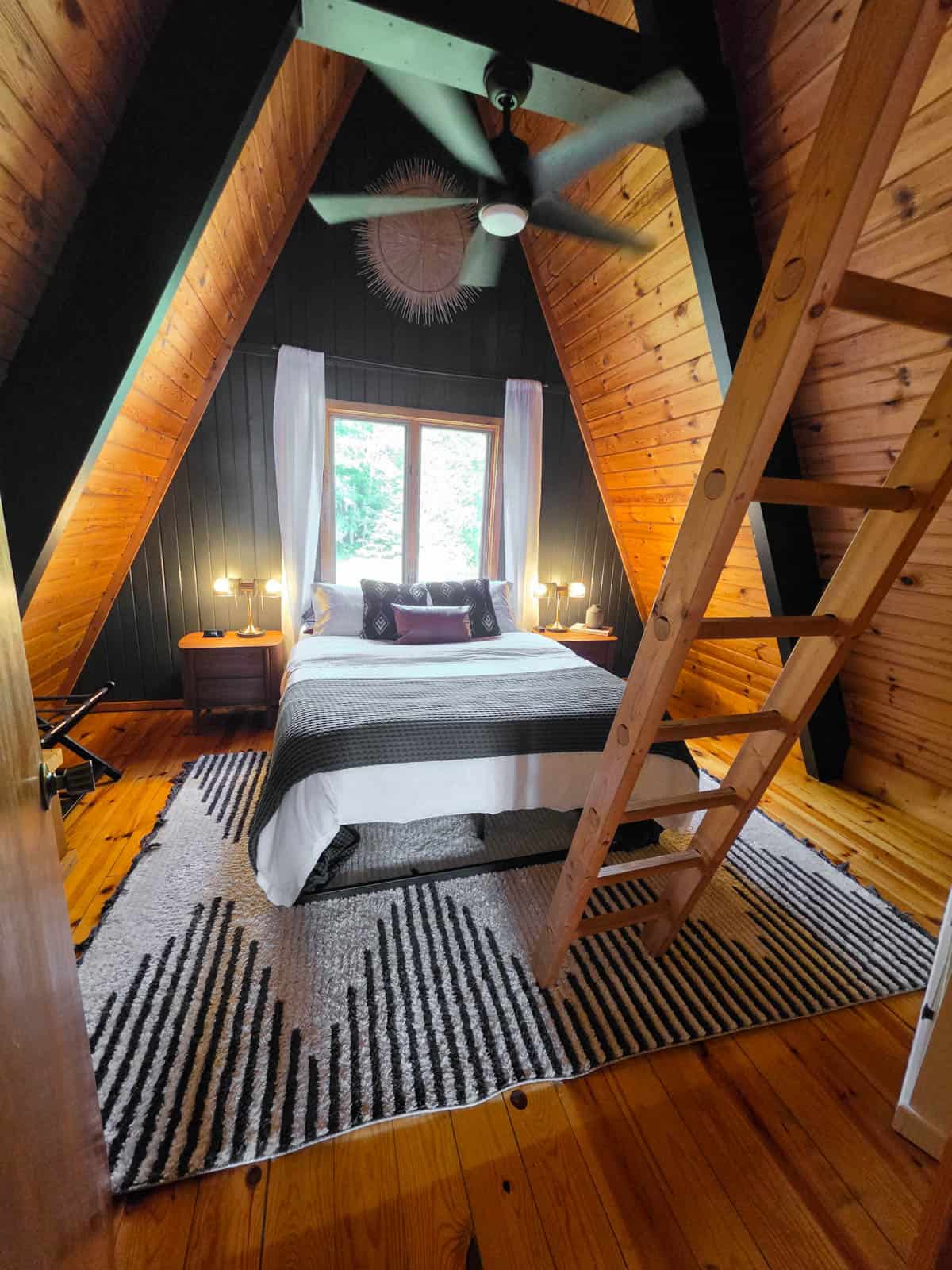 Cozy A-frame cabin bedroom with wood-paneled walls and loft ladder